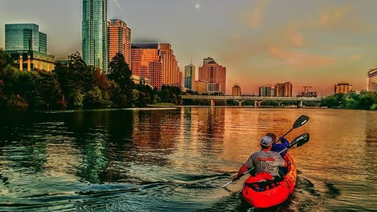 people kayaking in city lake during sunset